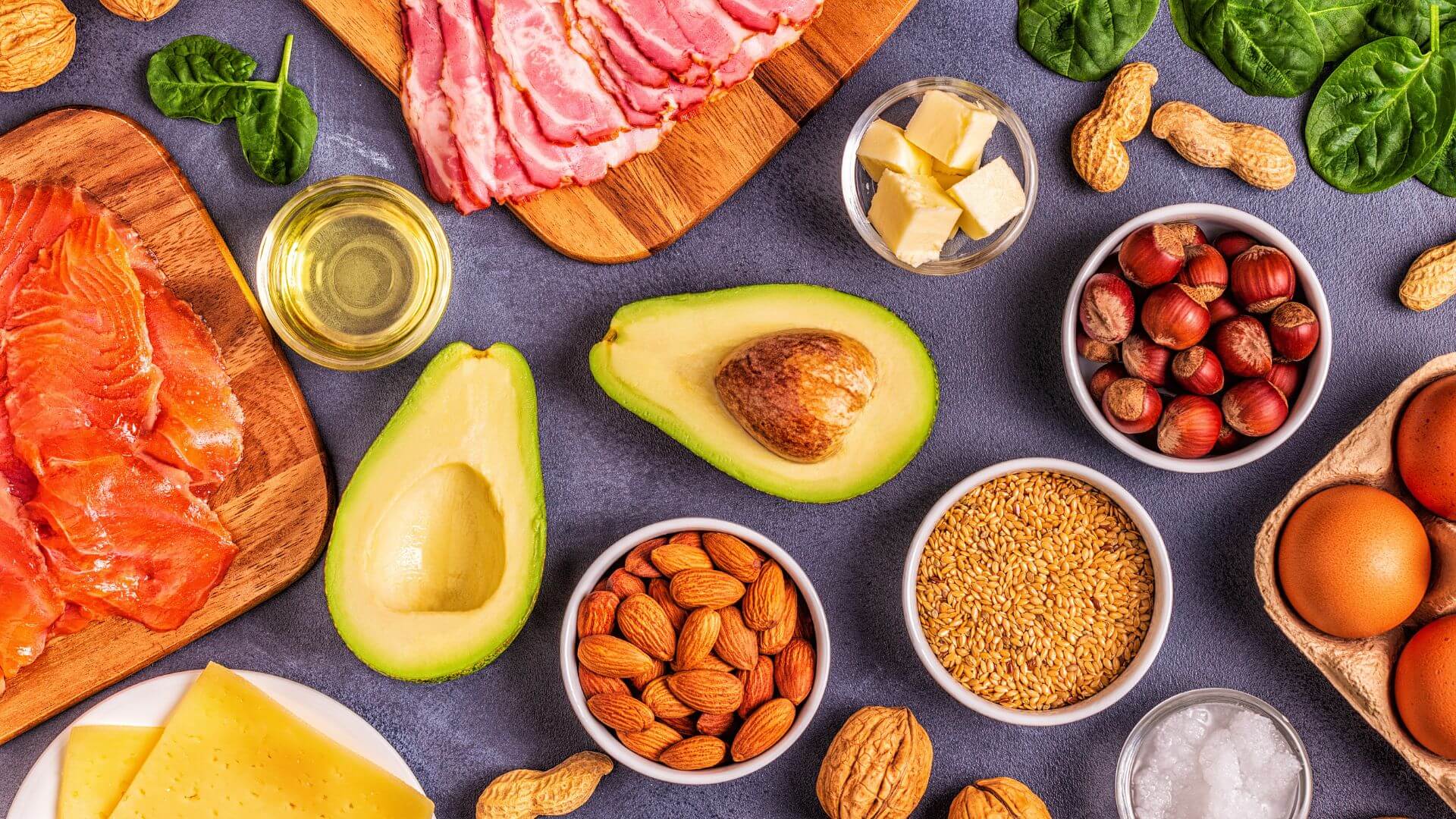 Aranjament văzut de sus cu alimente bogate în grăsimi și sărace în carbohidrați, specifice dietei Atkins: somon afumat, bacon, avocado, unt, brânză, ouă, alune, migdale, semințe de in și spanac