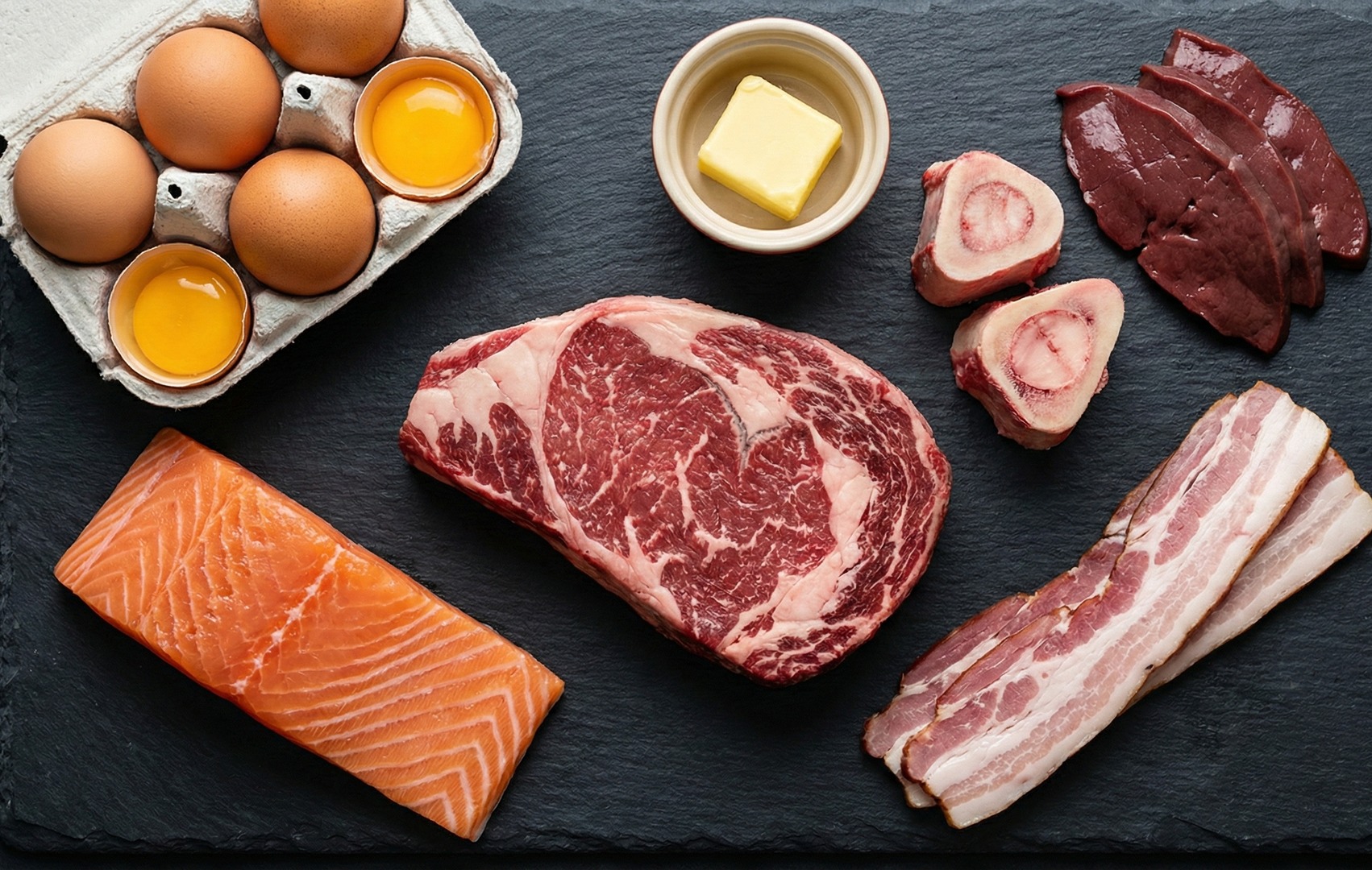 Selecție de carne și produse animale pentru dieta carnivoră: somon, vită marmorată, ouă, unt, oase cu măduvă, ficat și bacon